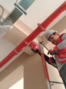 Técnico ajustando la abrazadera de una tubería contra incendio bajo un ducto