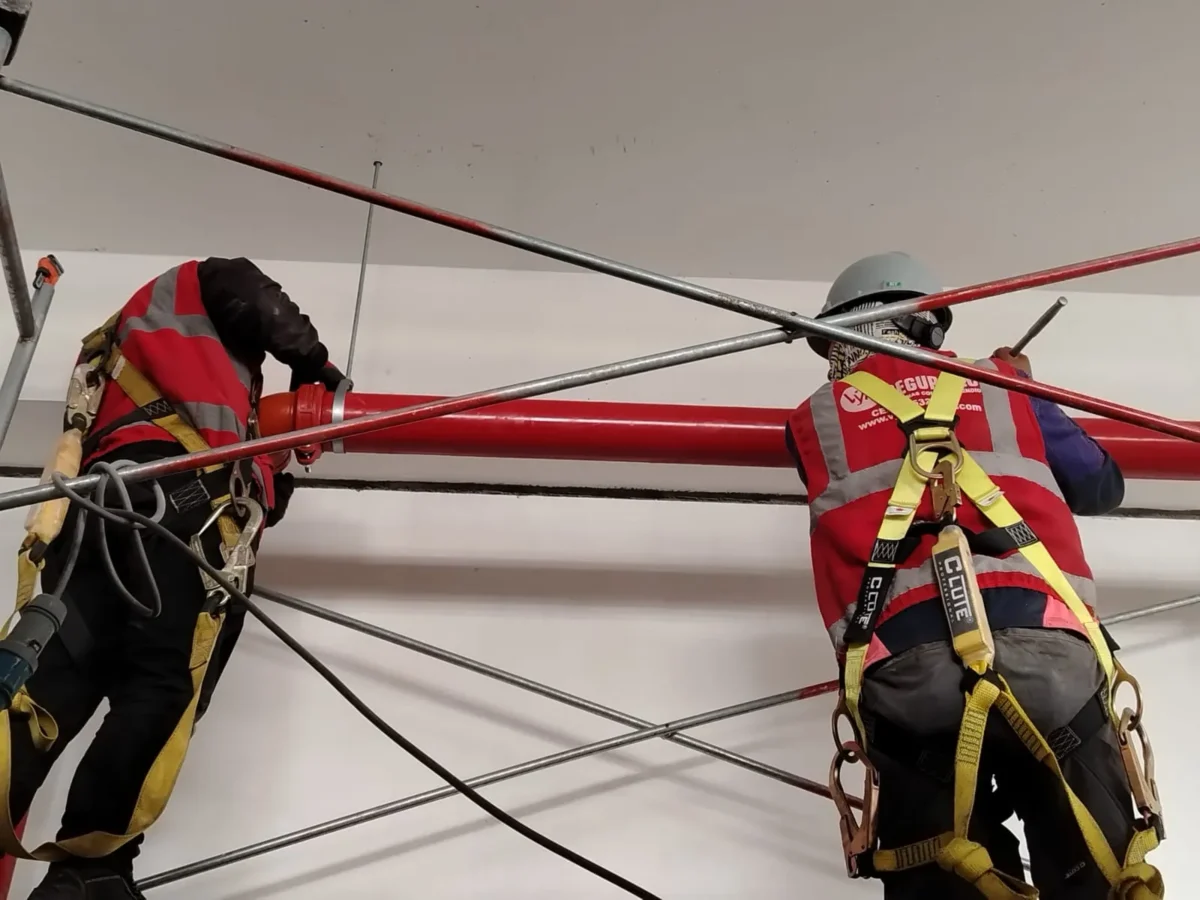 Técnicos con arnés alineando una tubería horizontal de agua contra incendio
