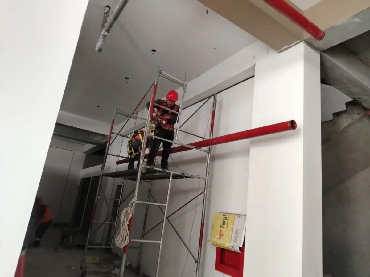 Técnicos en andamio de doble altura montando tubería contra incendio junto a una columna