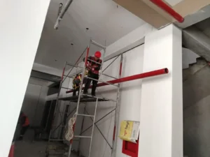 Técnicos en andamio de doble altura montando tubería contra incendio junto a una columna