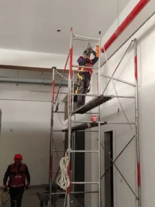 Técnico en andamio alto instalando tubería en un ambiente de doble altura