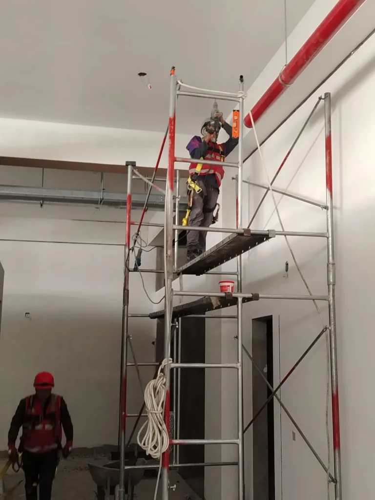 Técnico en andamio alto instalando tubería en un ambiente de doble altura