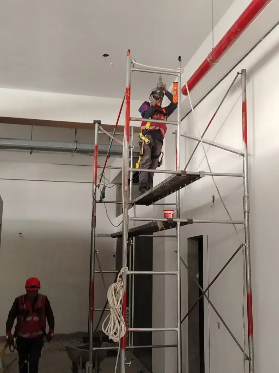 Técnico en andamio alto instalando tubería en un ambiente de doble altura