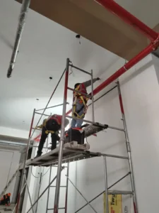 Técnicos en andamio con herramientas montando tubería en techo alto
