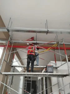 Técnico en andamio bajo la red de tubería contra incendio y bandejas