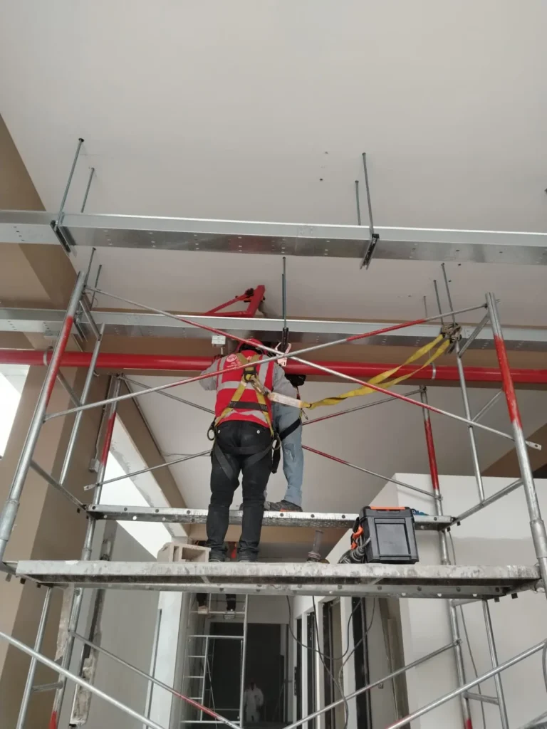 Técnico en andamio bajo la red de tubería contra incendio y bandejas