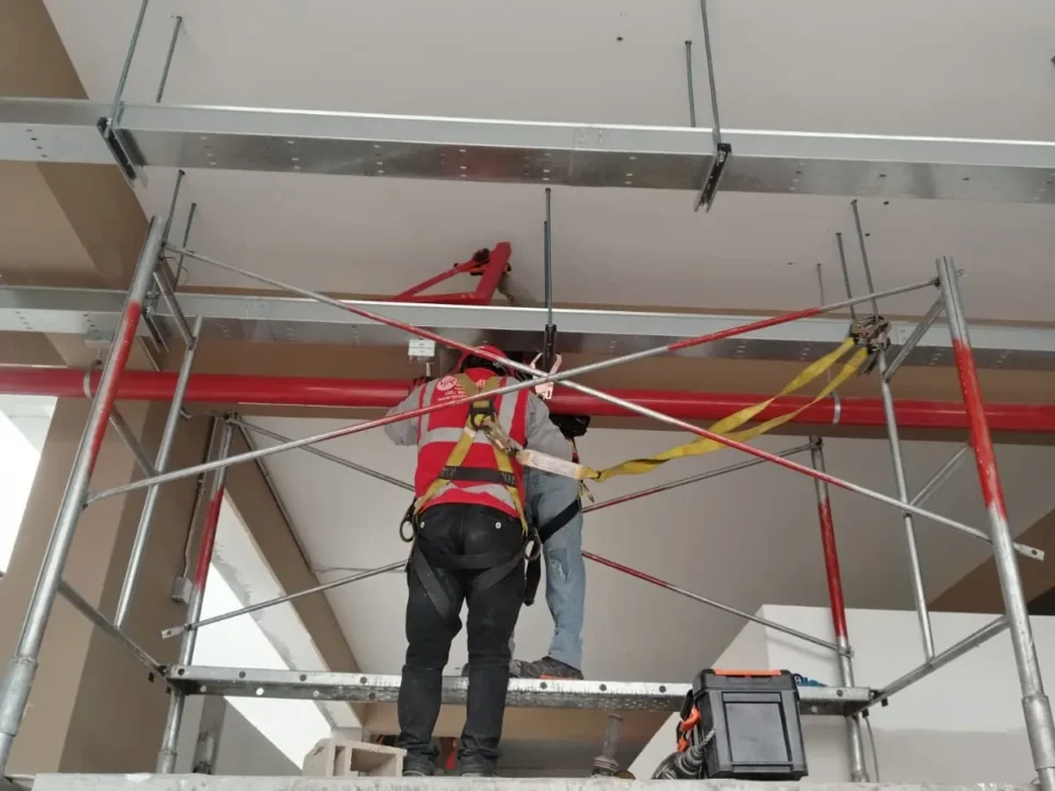 Técnico en andamio bajo la red de tubería contra incendio y bandejas