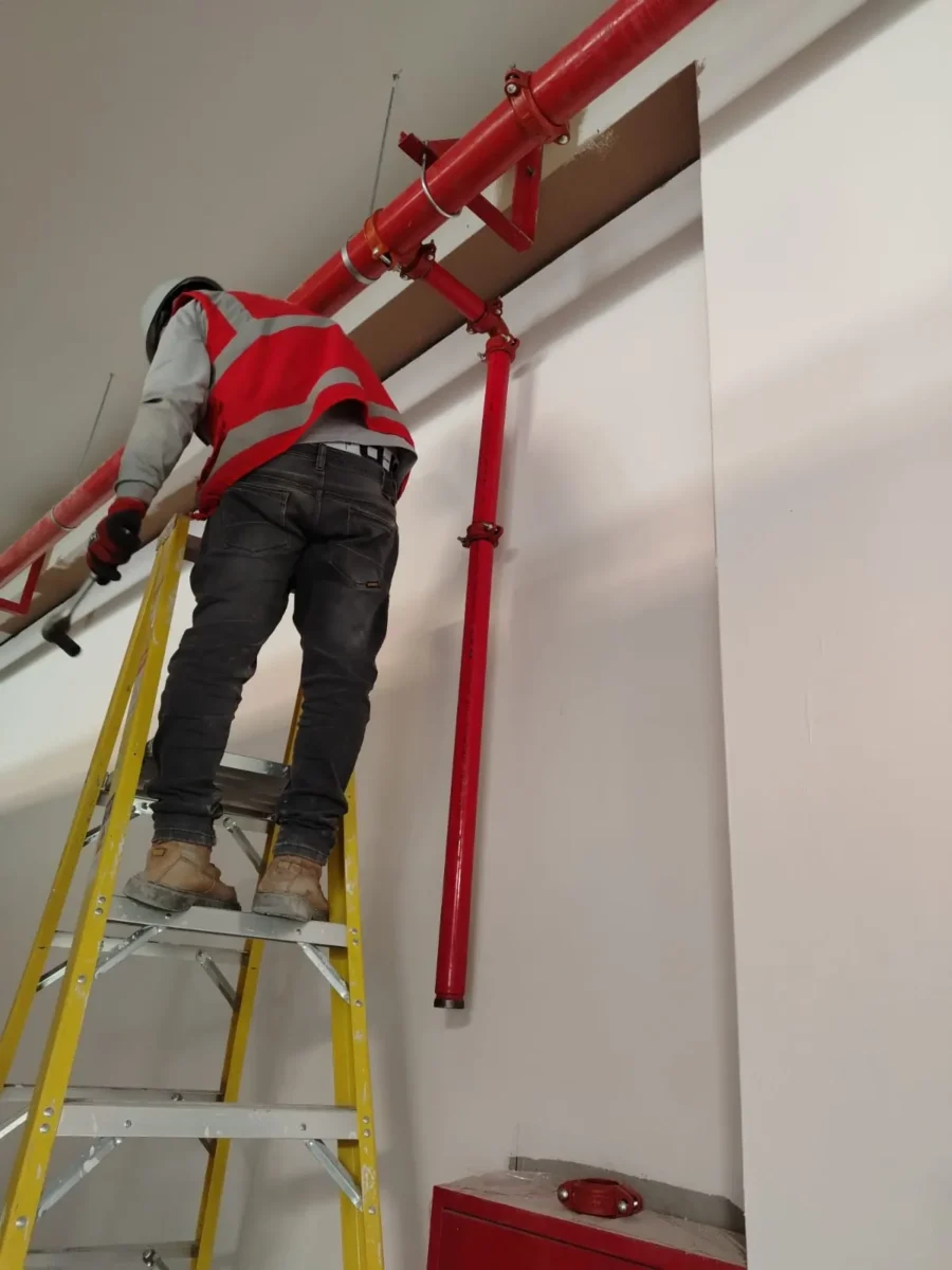 Técnico en escalera instalando la bajada de tubería contra incendio