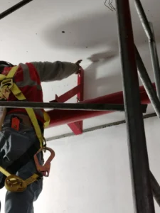Detalle de soporte metálico de tubería fijado a la pared por un técnico con arnés