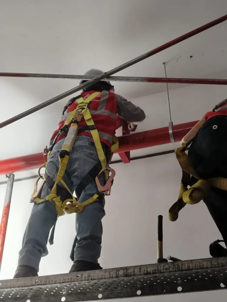 Técnicos con arnés fijando tubería horizontal en altura