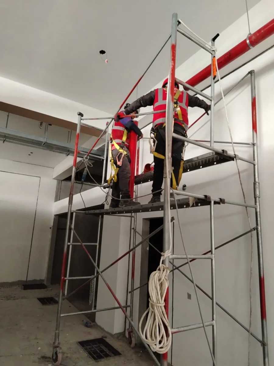 Técnicos en andamio montando tubería contra incendio en pared de doble altura