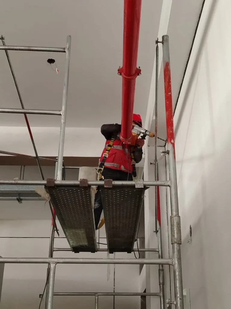 Técnico en andamio instalando un montante vertical de tubería roja
