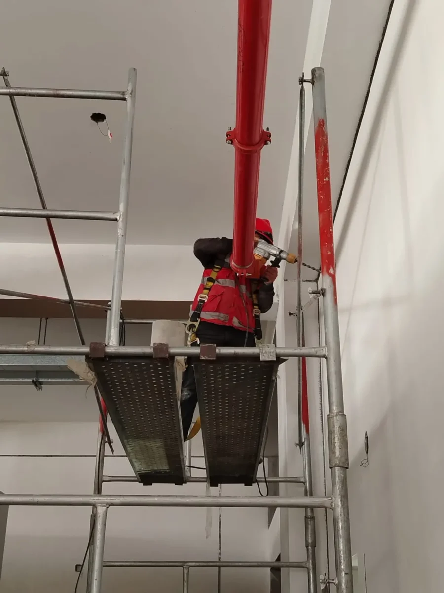 Técnico en andamio instalando un montante vertical de tubería roja