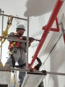 Técnico con casco y arnés perforando para el soporte de una tubería vertical
