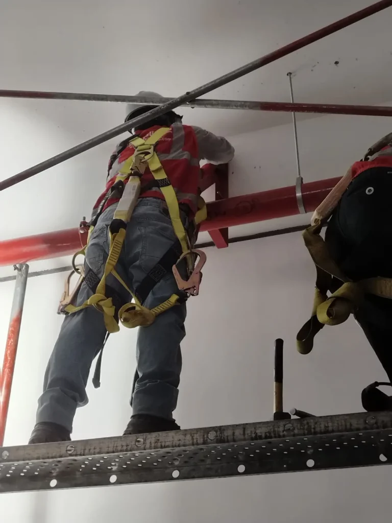 Técnico con arnés en plataforma fijando tubería contra incendio