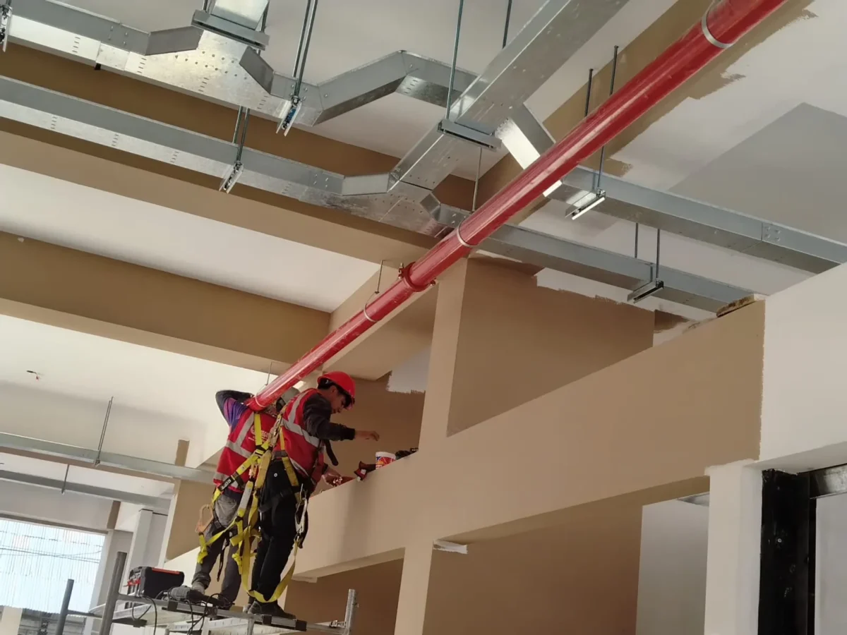 Red de tubería roja de agua contra incendio en techo con ductos y técnicos trabajando