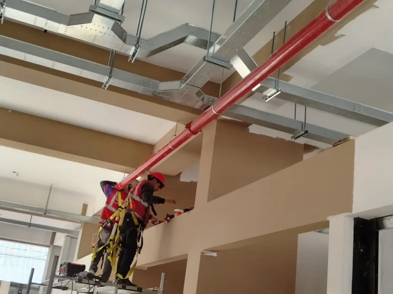 Red de tubería roja de agua contra incendio en techo con ductos y técnicos trabajando