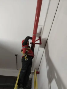 Técnico en escalera fijando el soporte de una tubería en pared alta