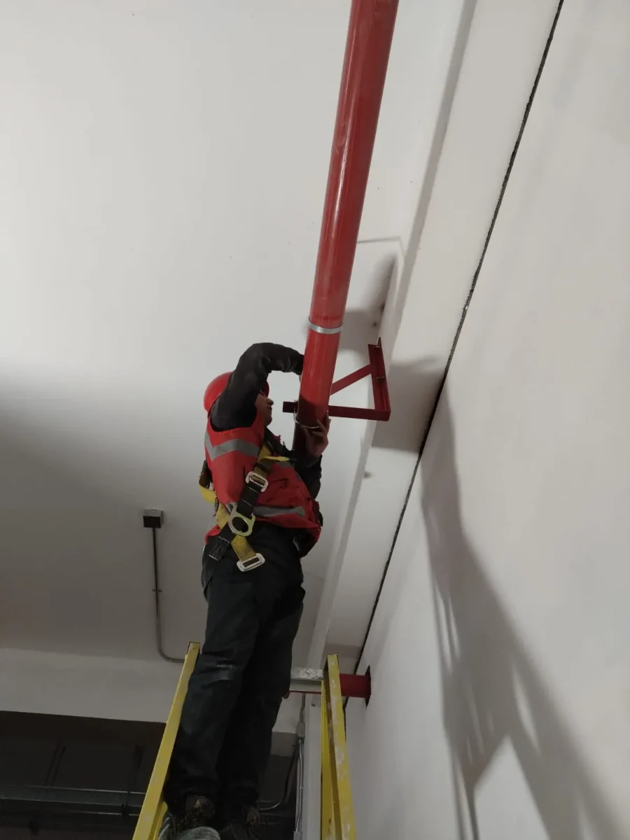 Técnico en escalera fijando el soporte de una tubería en pared alta