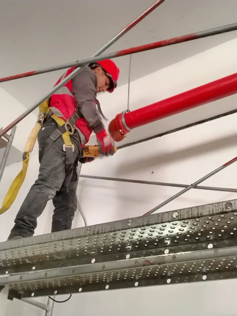 Técnico con arnés en andamio ajustando un tramo de tubería roja