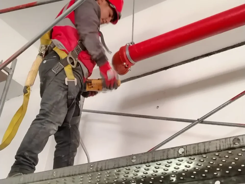 Técnico con arnés en andamio ajustando un tramo de tubería roja