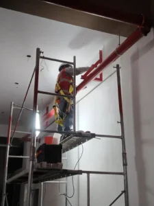 Técnico con arnés en andamio fijando tubería roja a la pared
