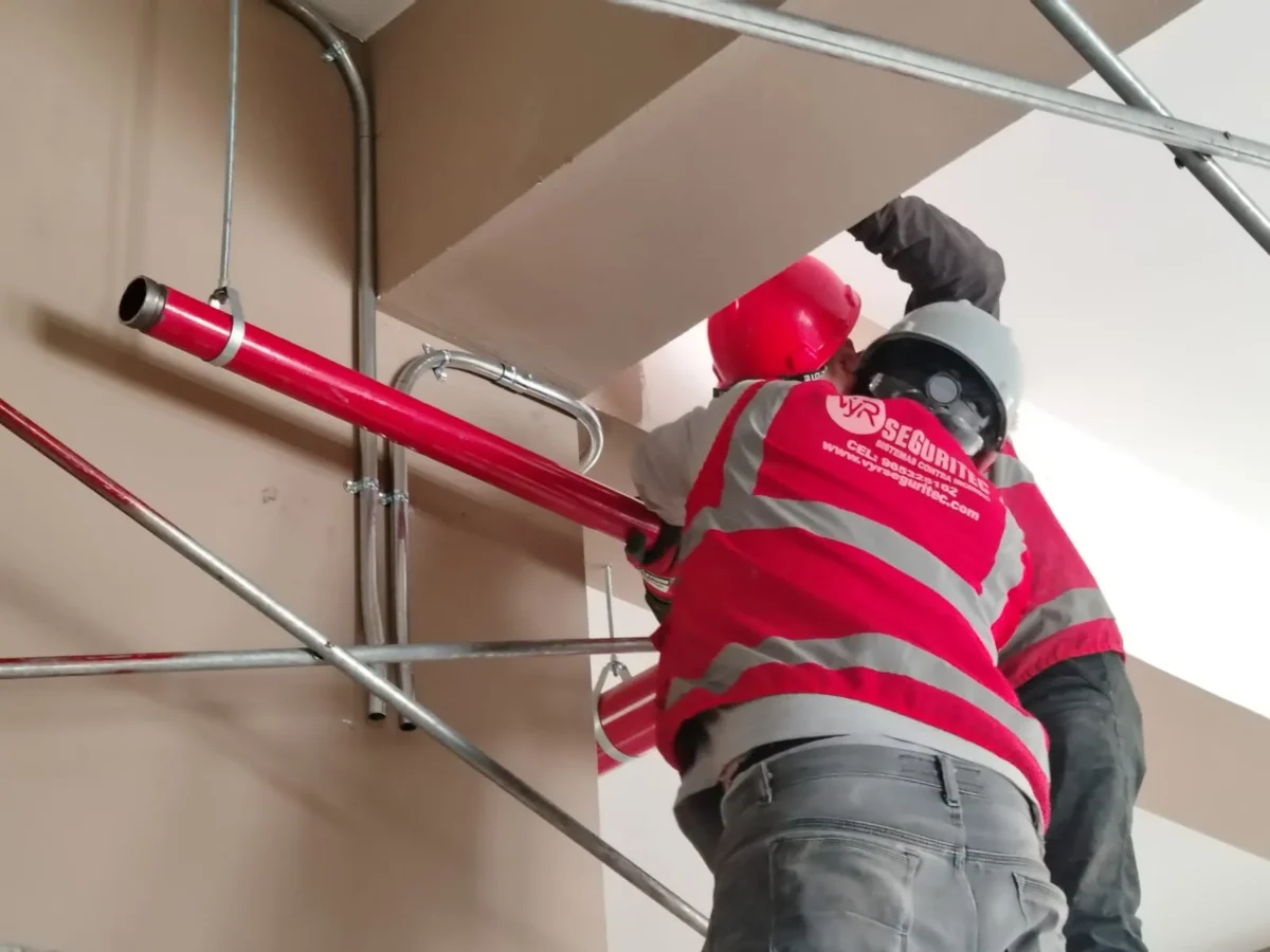 Dos técnicos instalando un tramo de tubería roja junto a bandejas eléctricas