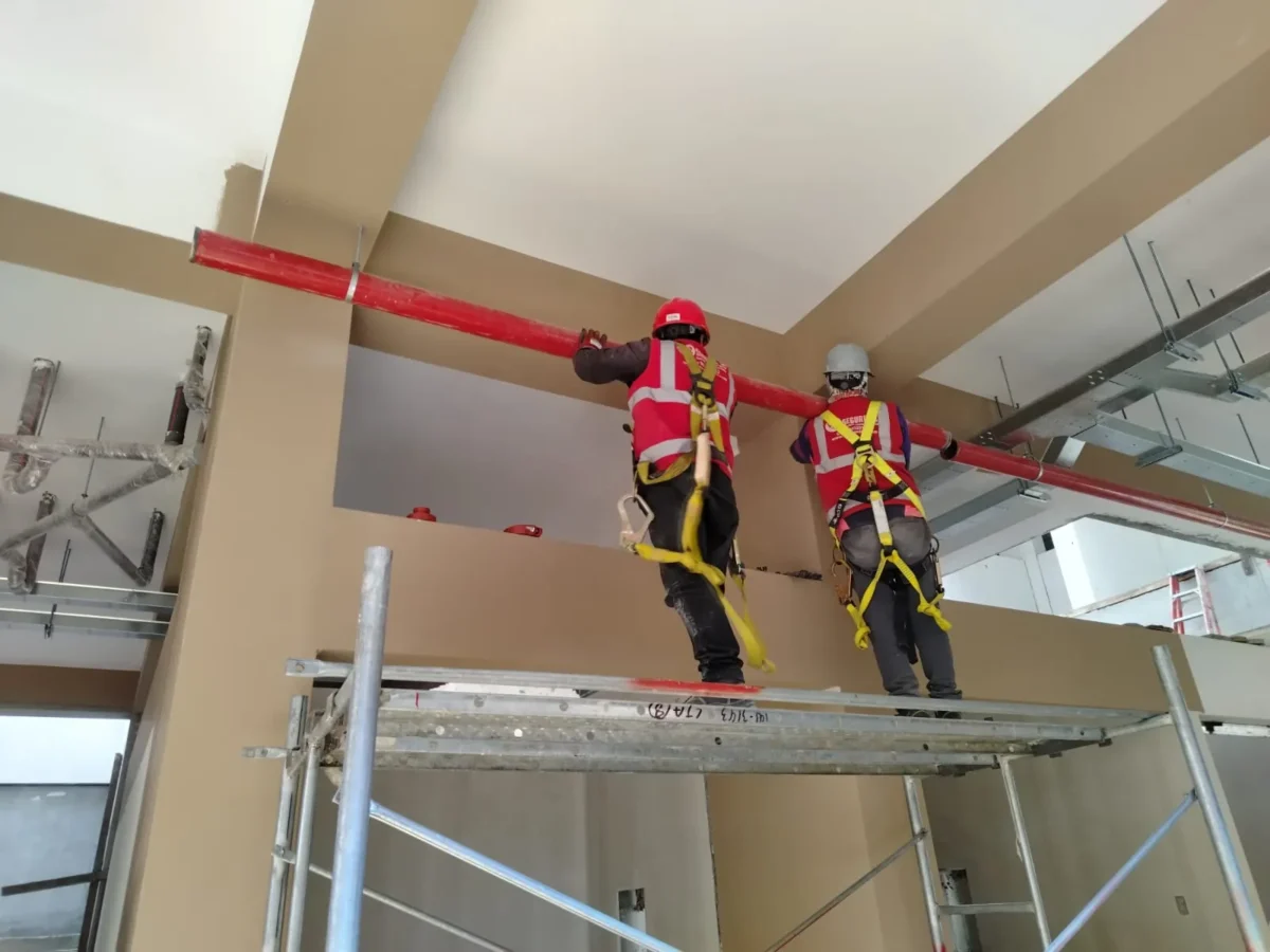 Dos técnicos en andamio instalando tubería a lo largo de una viga