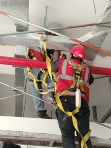 Técnicos con arnés montando tubería bajo bandejas metálicas