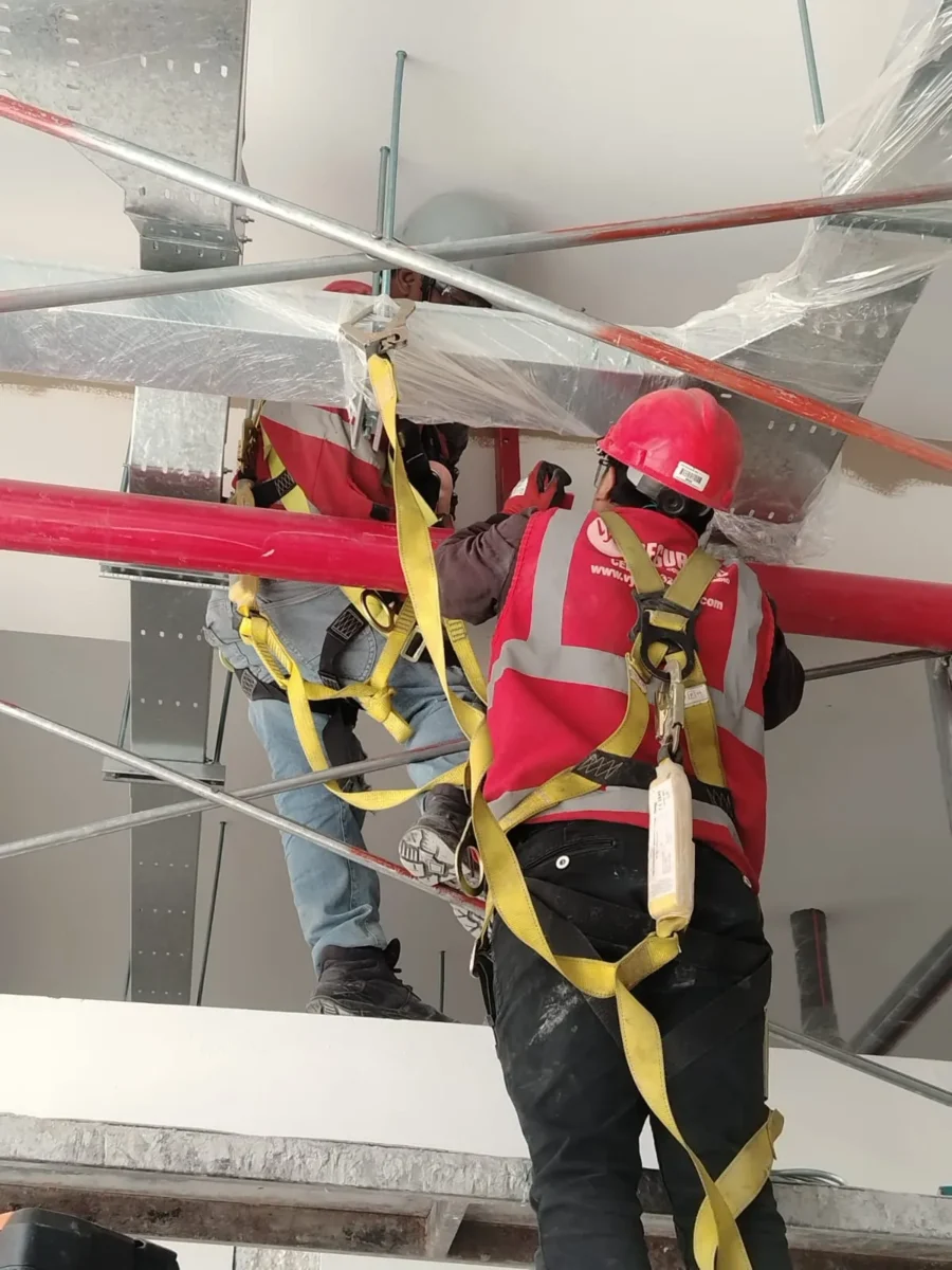 Técnicos con arnés montando tubería bajo bandejas metálicas