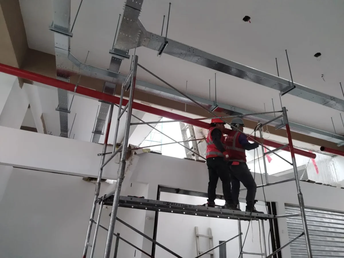 Técnicos con equipo de seguridad montando tubería roja entre ductos de ventilación