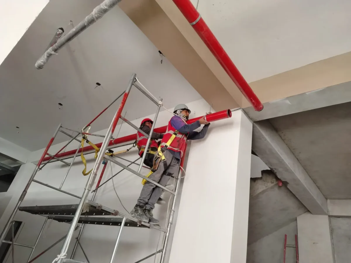Técnicos en andamio instalando tubería roja en la esquina de una viga