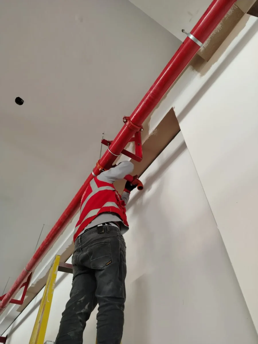 Técnico en escalera fijando tubería roja con su soporte