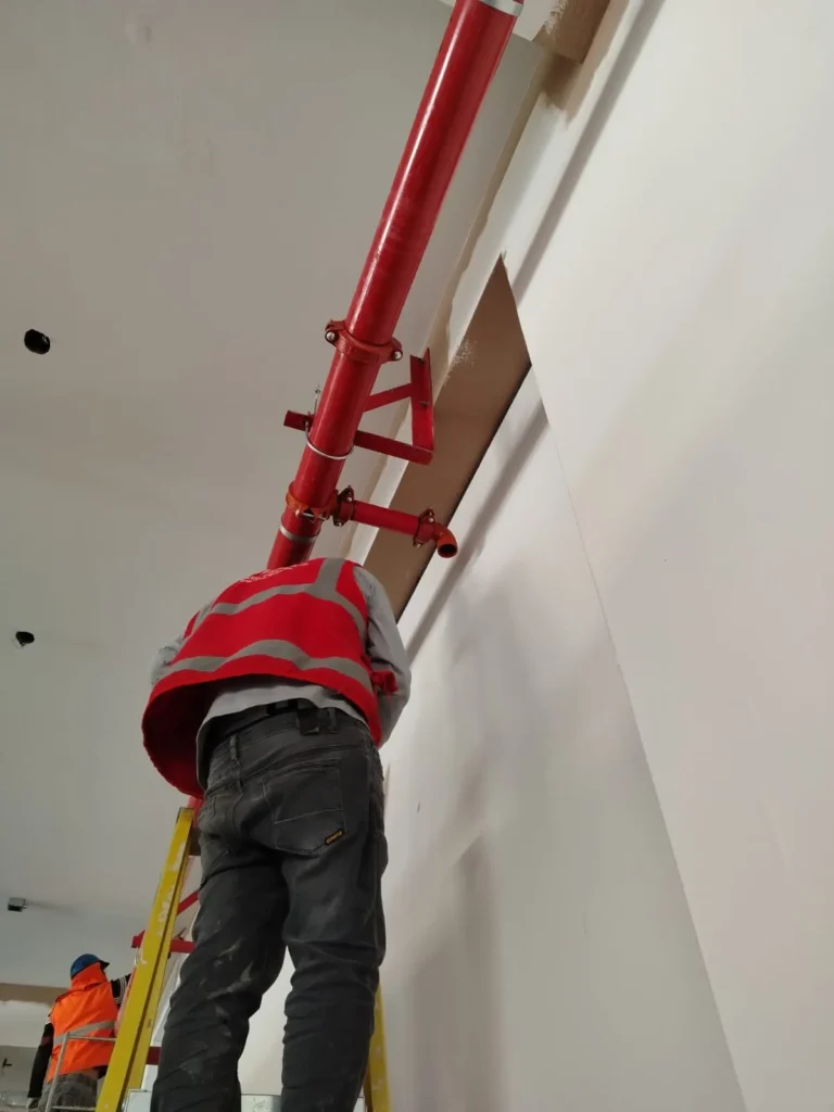 Técnico con chaleco rojo ajustando tubería contra incendio y su soporte en la pared