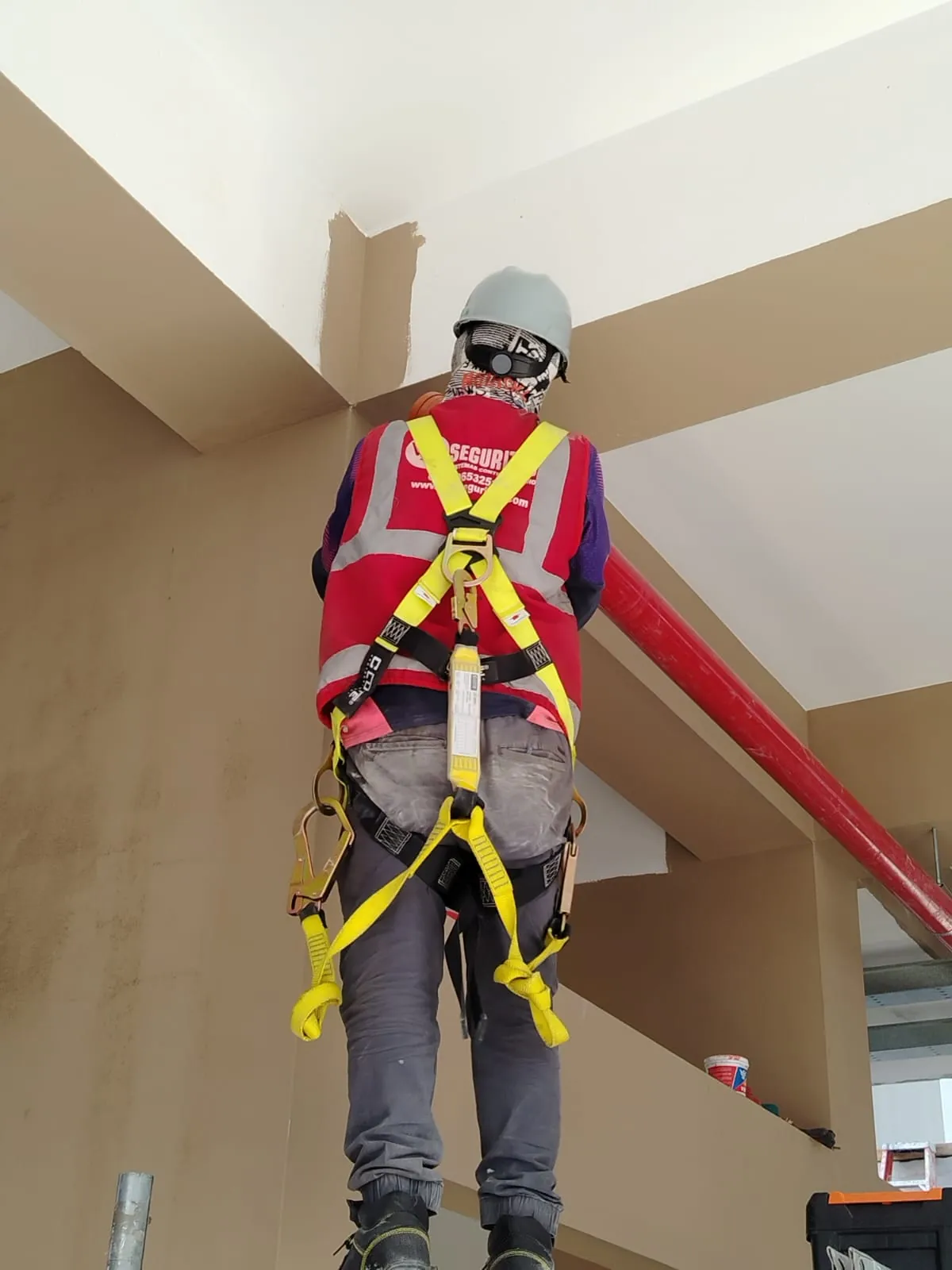 Técnico con casco y arnés de seguridad trabajando en altura junto a la tubería roja de un sistema contra incendio