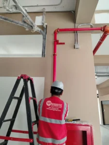 Técnico de VYR SEGURITEC con casco y chaleco instalando la bajada de tubería a un gabinete contra incendio