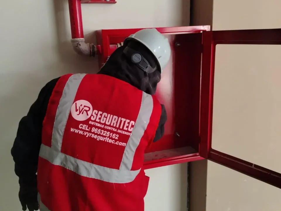 Técnico de VYR SEGURITEC revisando la conexión de un gabinete contra incendio con la puerta de vidrio abierta