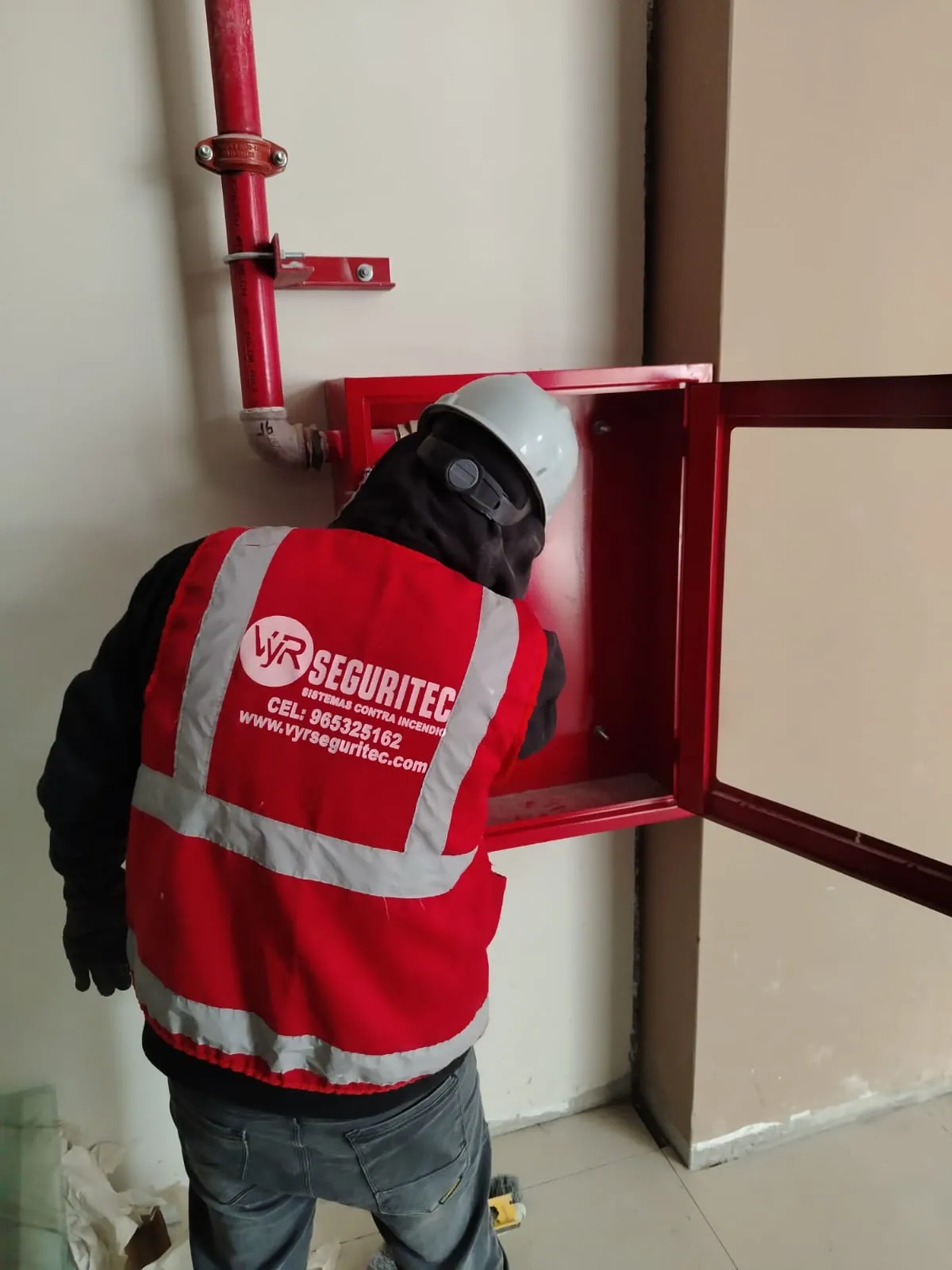 Técnico de VYR SEGURITEC revisando la conexión de un gabinete contra incendio con la puerta de vidrio abierta